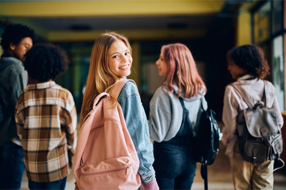 Schülerin mit rosa Rucksack lächelt, im Hintergrund Mitschüler